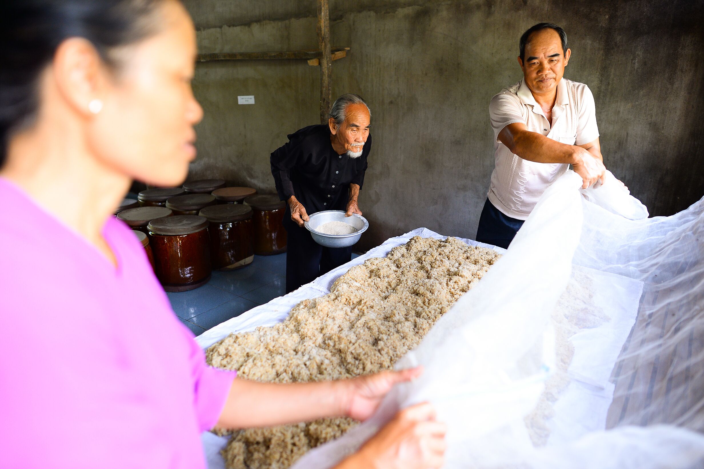 A group of people handling large bags of food in a rustic setting with barrels in the background.