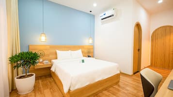 Habitación de hotel con cama, mesita de noche, lámpara, planta en maceta y armario de madera.