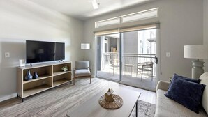 A modern living room with a flat-screen TV, a sofa, a coffee table, and a balcony with outdoor furniture.