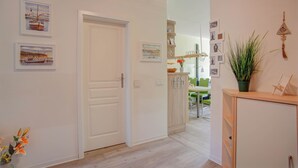 Un couloir avec une porte blanche, un meuble en bois orné d’une plante et des œuvres d’art accrochées aux murs.