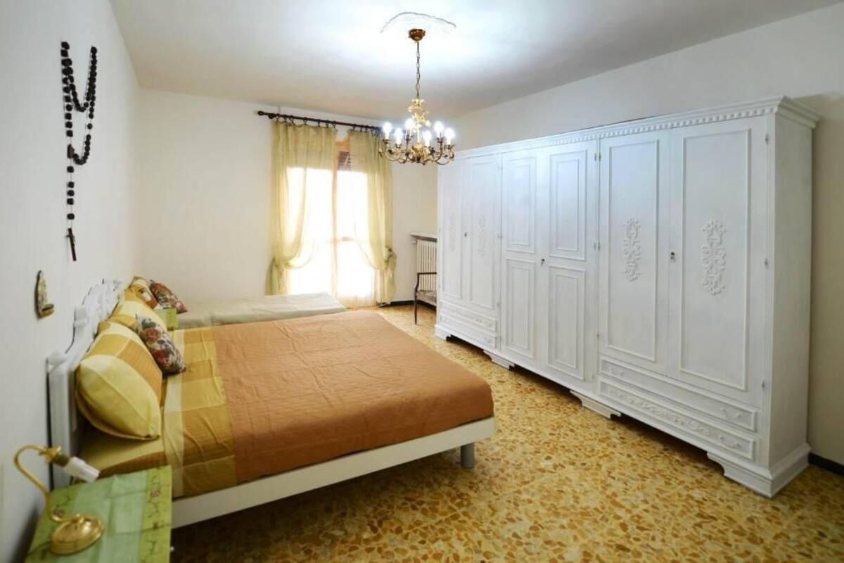 Een slaapkamer met een bed, een kledingkast, een kroonluchter en een raam met gordijnen.