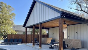 A covered patio with lounge chairs, a pool, and a wooden fence.