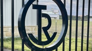 A metal gate with a circular emblem featuring a stylized letter 'R'.