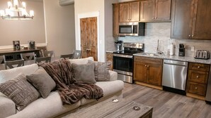A modern kitchen with wooden cabinets, stainless steel appliances, and a dining area with a sofa and coffee table.