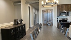 A modern kitchen with a dining area, featuring a long wooden table, dark cabinetry, and stainless steel appliances.