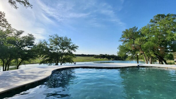 A swimming pool with a curved edge, surrounded by trees and a clear sky.