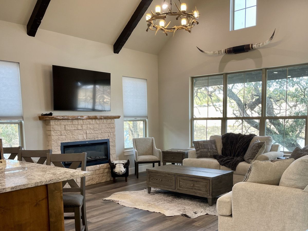A spacious living room with a stone fireplace, comfortable seating, a large TV, and large windows offering natural light and views.