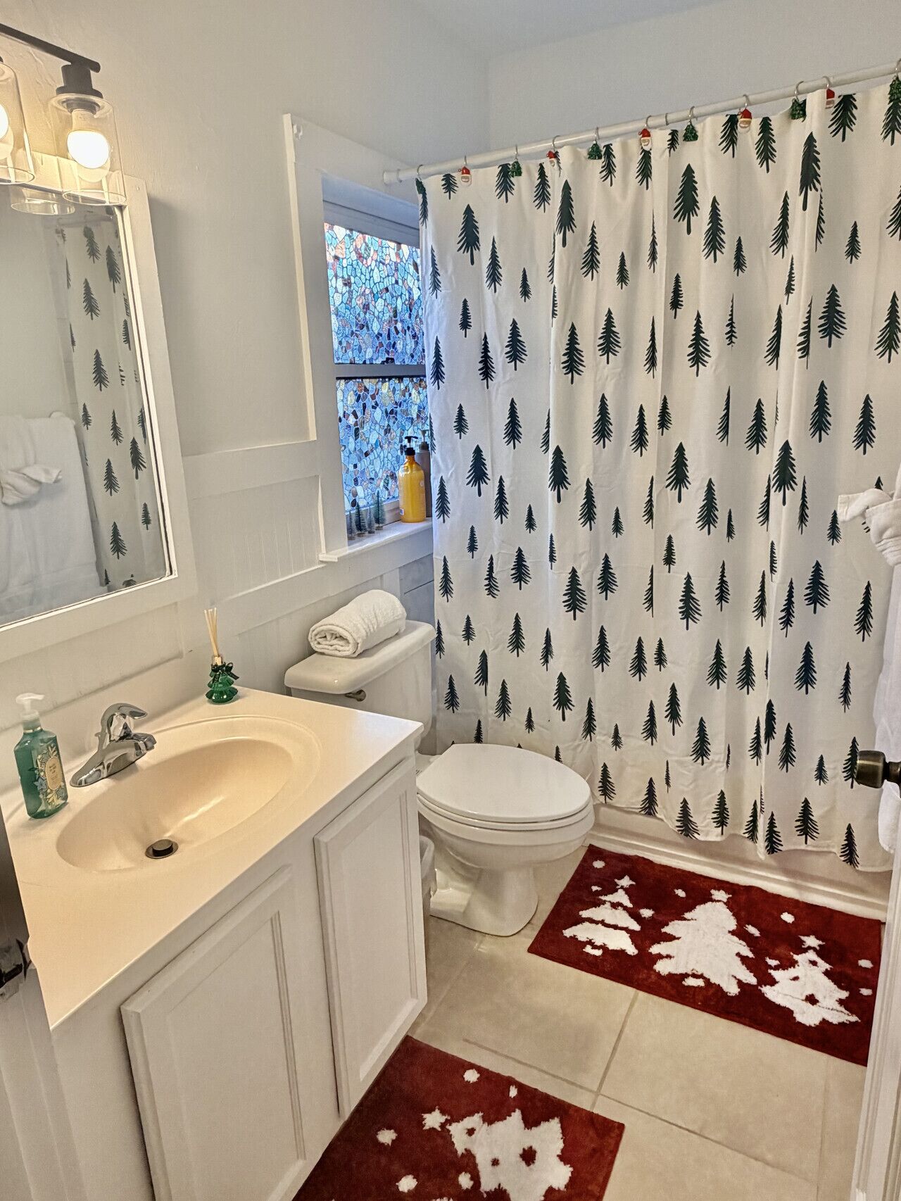 Une salle de bain avec un lavabo blanc, un miroir et des toilettes. Il y a un rideau de douche orné d’un motif représentant un arbre.