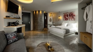 A modern hotel room with a sofa, a bed, a TV, a coffee machine, and artwork on the walls.