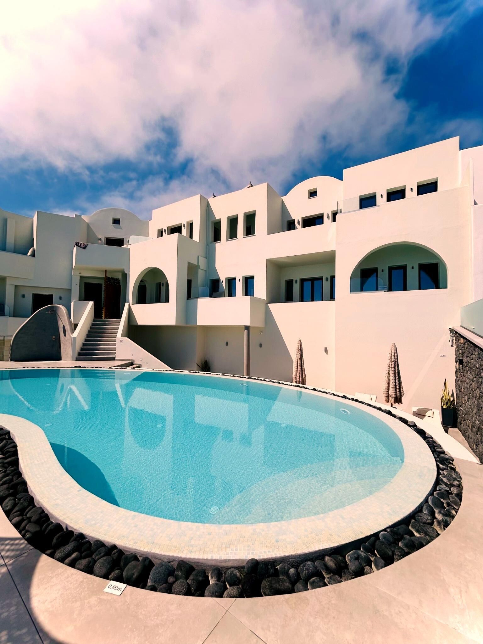 A modern building with a pool, stone walls, and a clear sky.
