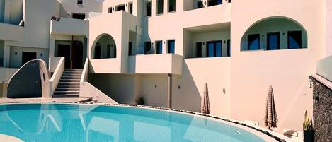 A modern building with a pool, stone walls, and a clear sky.