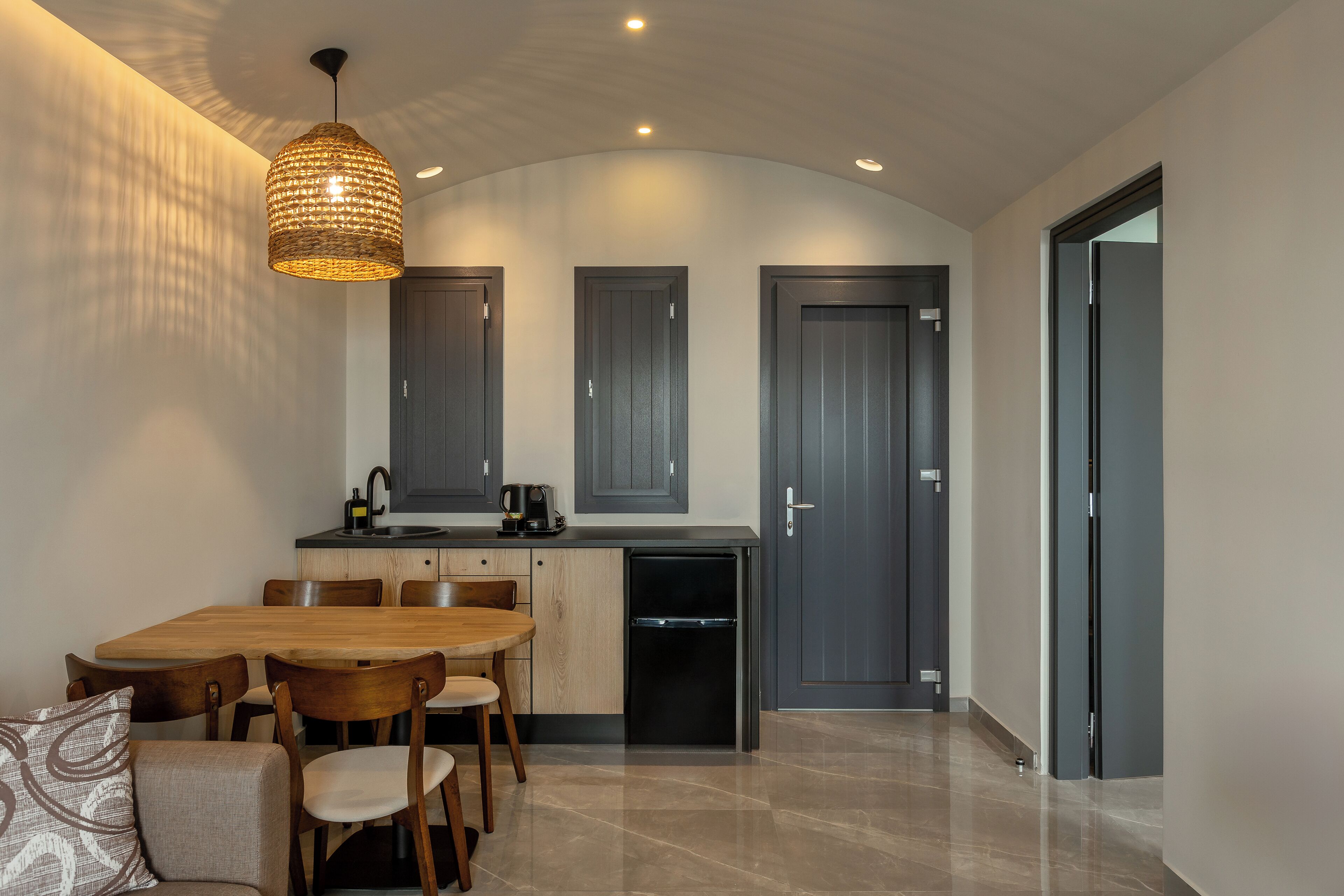 A modern kitchen with a dining area, featuring a wooden table, chairs, a built-in dishwasher, and a hanging light fixture.