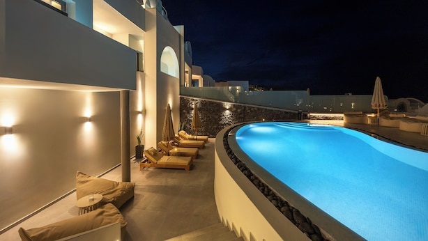 A modern pool area with lounge chairs and umbrellas, surrounded by a white building with stone accents.