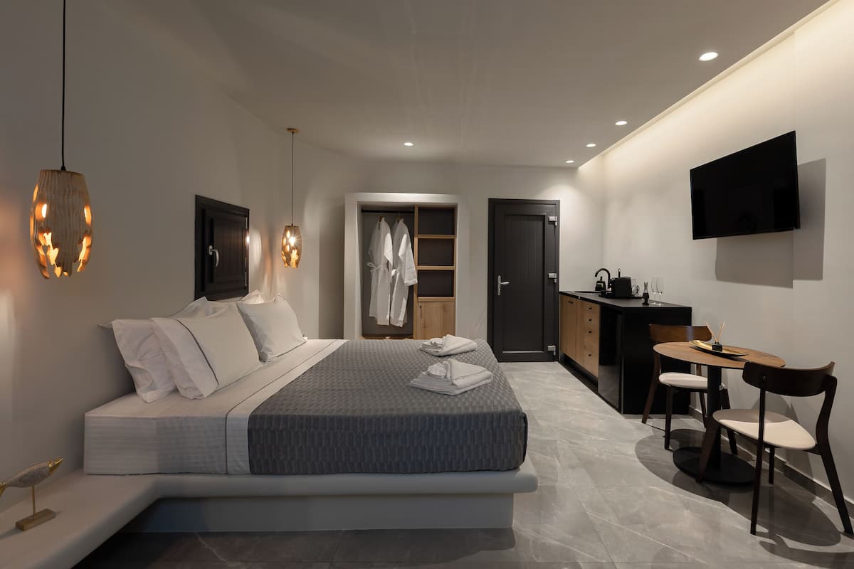 A modern hotel room with a large bed, a desk with a chair, a wardrobe, and a TV mounted on the wall.