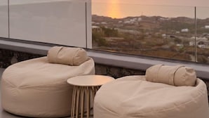 A modern outdoor seating area with a view of the sunset over the sea.