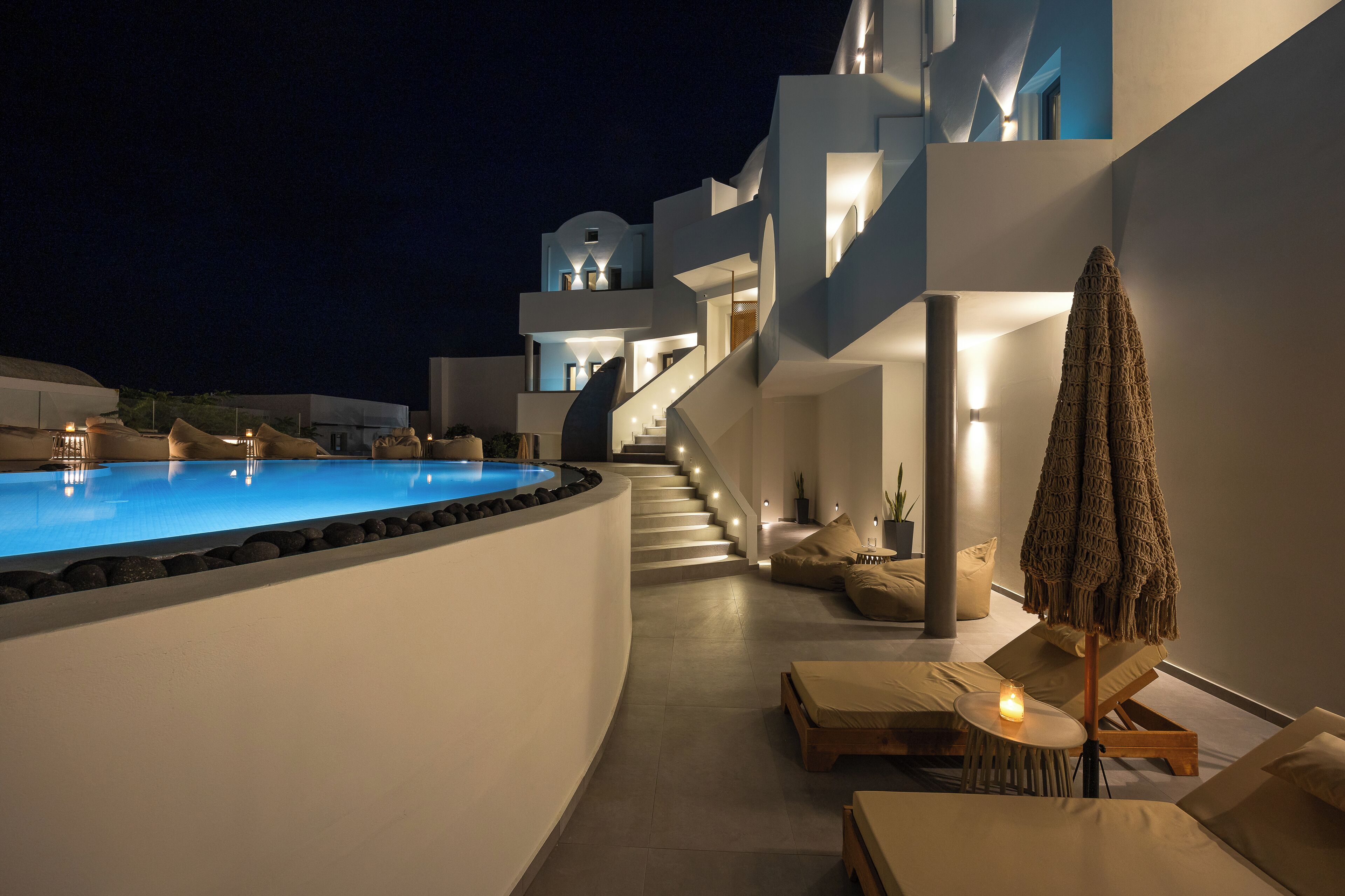 A modern hotel with a swimming pool, outdoor seating, and a staircase leading to upper floors.