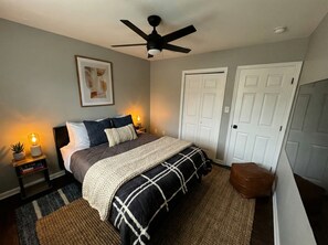 A bedroom with a bed, bedside lamps, a ceiling fan, and a door. - Renovated 3BR — King Suite, Laundry, Parking (New Castle)