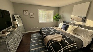 A bedroom with a bed, dresser, TV, and artwork on the walls. - Renovated 3BR — King Suite, Laundry, Parking (New Castle)