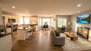 A modern kitchen with an island, dining area with chairs, a sofa, and a fireplace. - Renovated 3BR — King Suite, Laundry, Parking (New Castle)