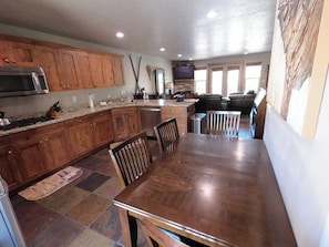 A kitchen with wooden cabinets, a dining table with chairs, a microwave, and a TV mounted on the wall. - 3 BR 3.5bth with 2 En-Suite King Bedrooms (Eden)