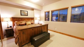 A bedroom with a wooden bed, bedside lamps, a bench, and windows with blinds. - 3 BR 3.5bth with 2 En-Suite King Bedrooms (Eden)