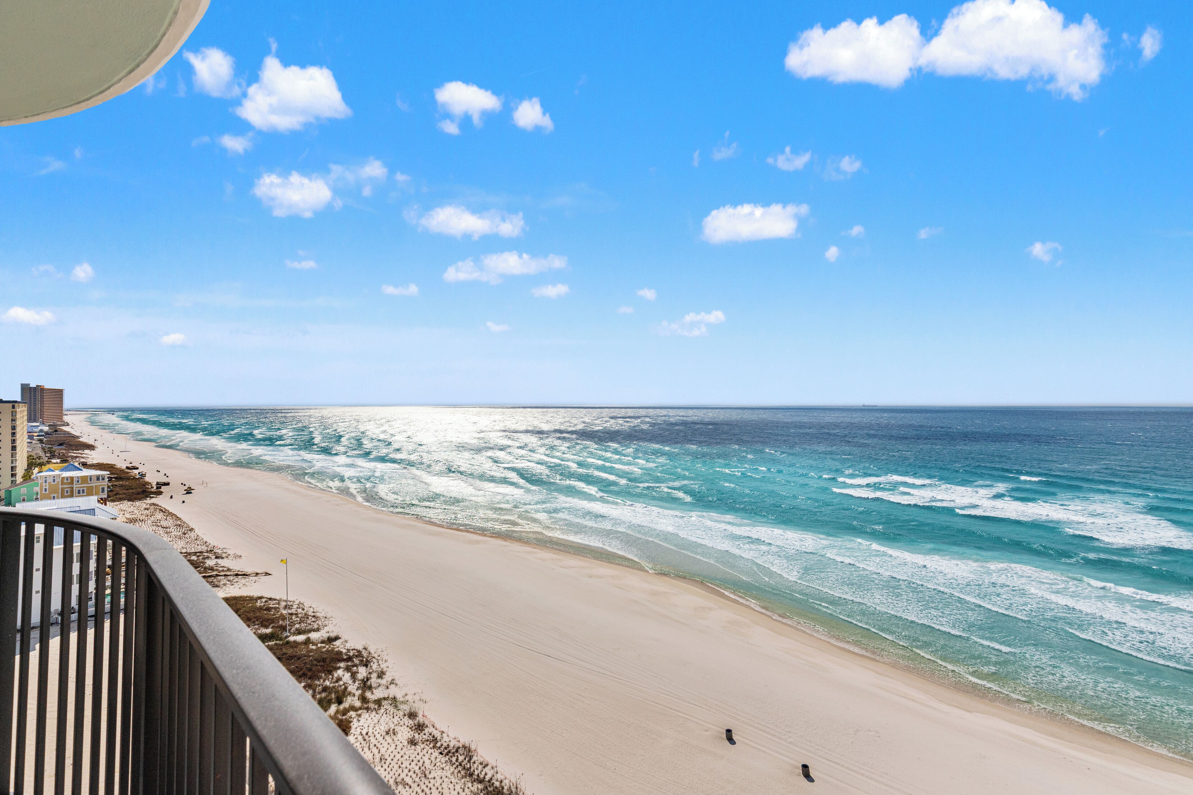 A beach with a clear sky, waves, and a few people walking.