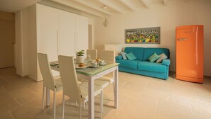 A dining area with a table, chairs, and a kitchen counter. There is a teal sofa and an orange refrigerator in the background. - BOUTIQUE HOTEL HISTORIC CENTER LECCE (Lecce)