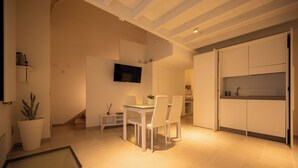 A modern kitchen with white cabinets, a dining table with chairs, a flat-screen TV mounted on the wall, and a potted plant. - BOUTIQUE HOTEL HISTORIC CENTER LECCE (Lecce)