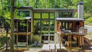Une cabane moderne à deux étages, dotée de grandes fenêtres, d’une terrasse et d’une cheminée.