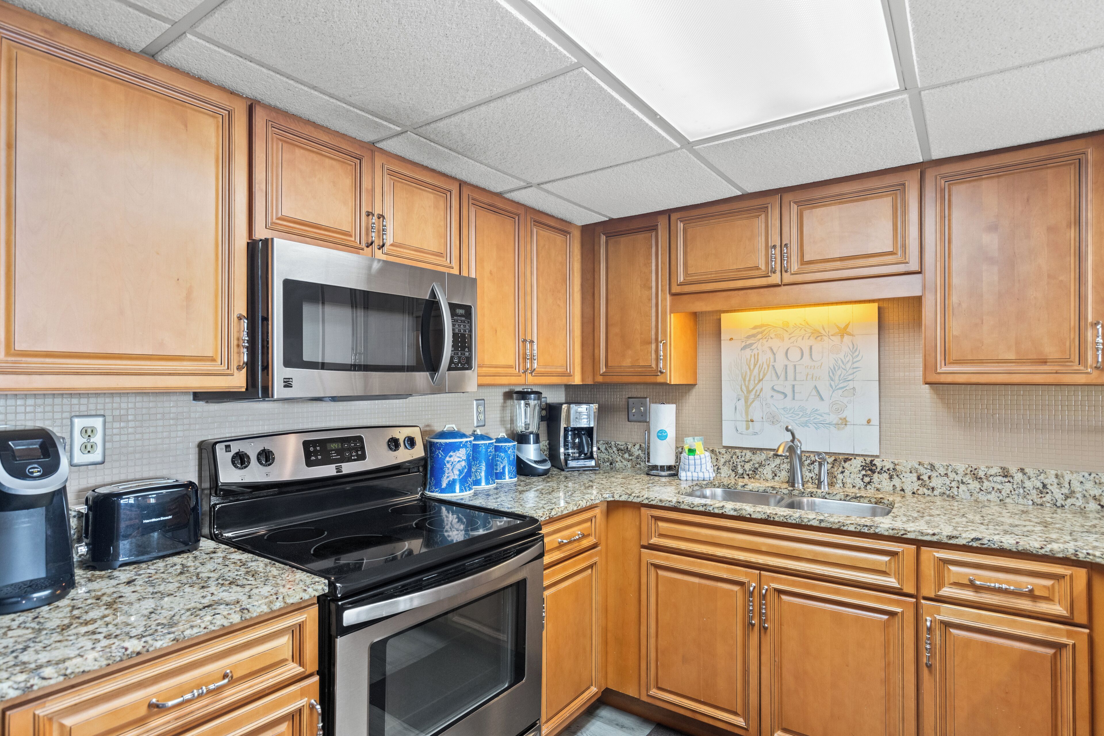 A kitchen with wooden cabinets, a stainless steel microwave, a stove, a sink, and a coffee maker.