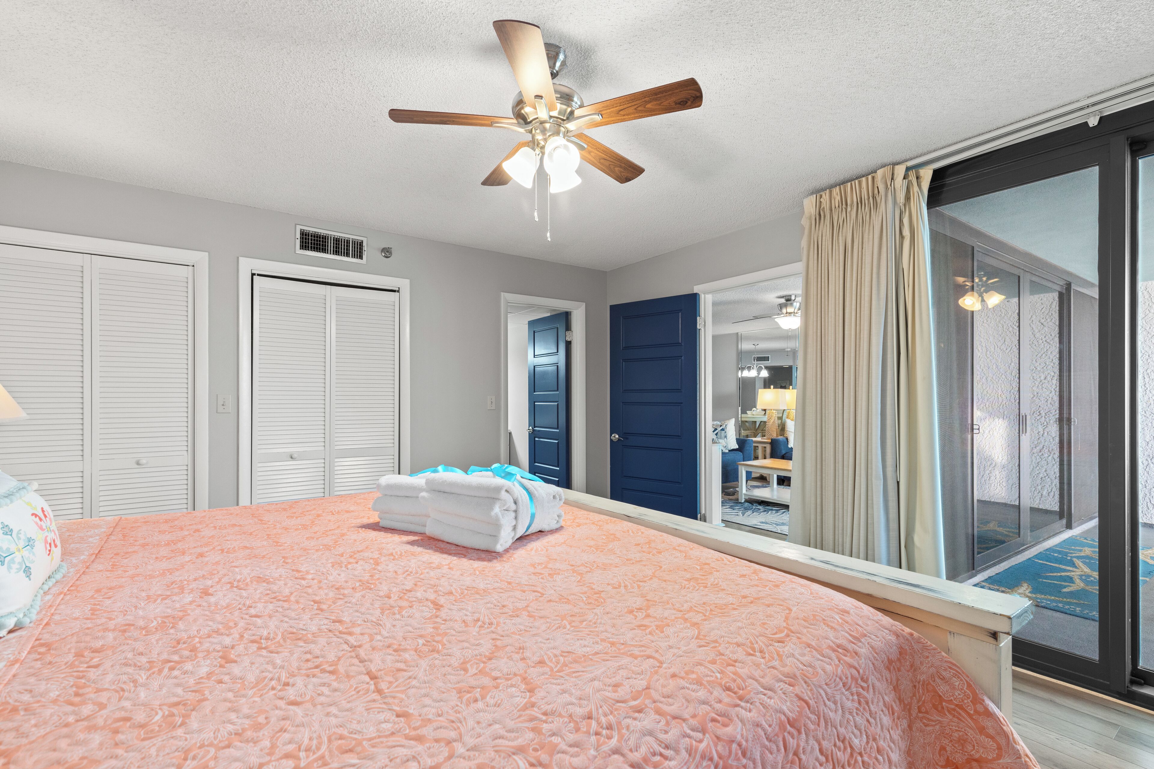 A hotel room with a large bed, a ceiling fan, and a view of the outside.