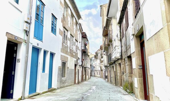 Calle estrecha bordeada por edificios con puertas azules y fachadas de piedra.