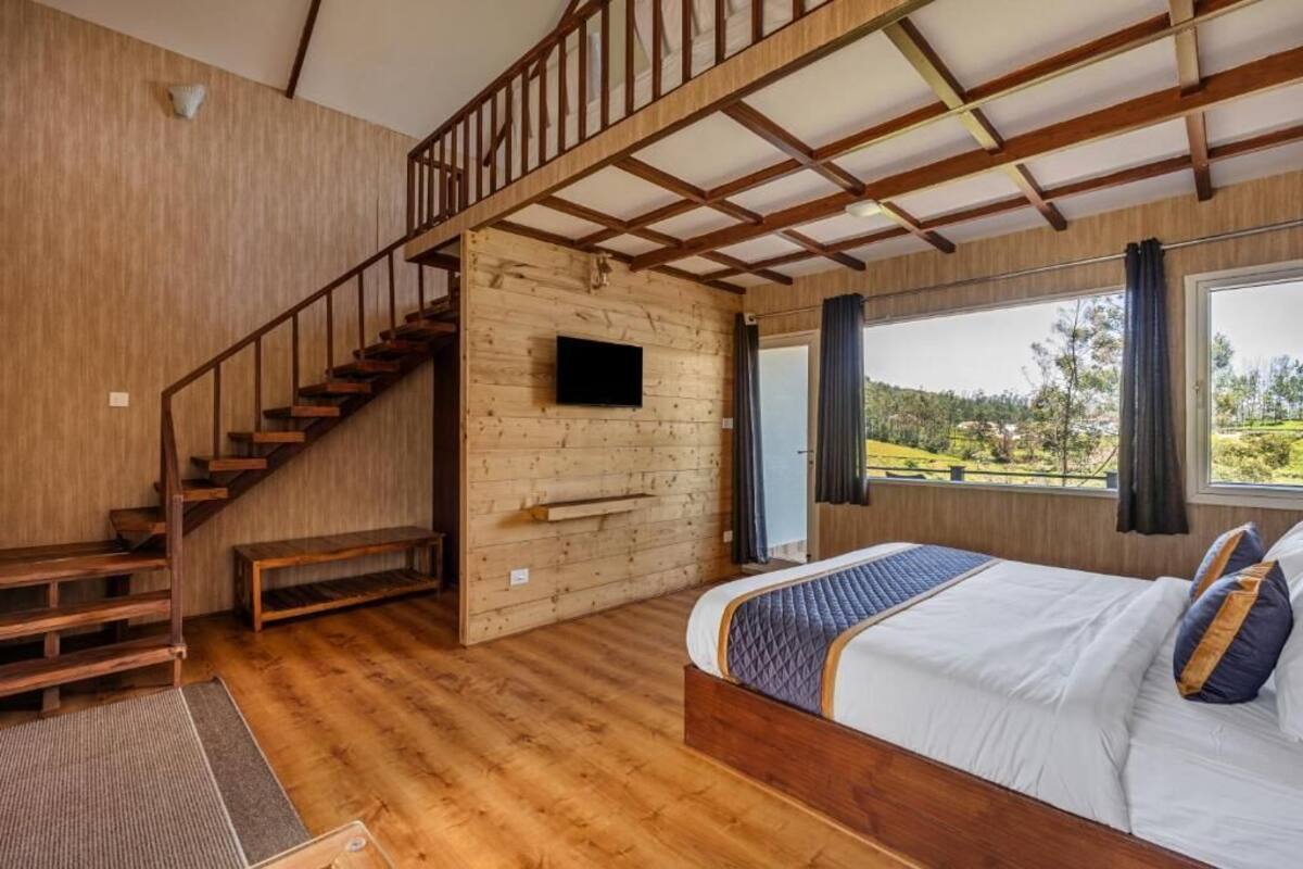 Une chambre avec un plancher en bois, un lit doté d’une tête de lit matelassée, un escalier en bois et un téléviseur fixé au mur.