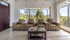 A living room with a sofa set, a coffee table, and large windows offering a view of greenery. - Wattle Grove Resort (Kotagiri)