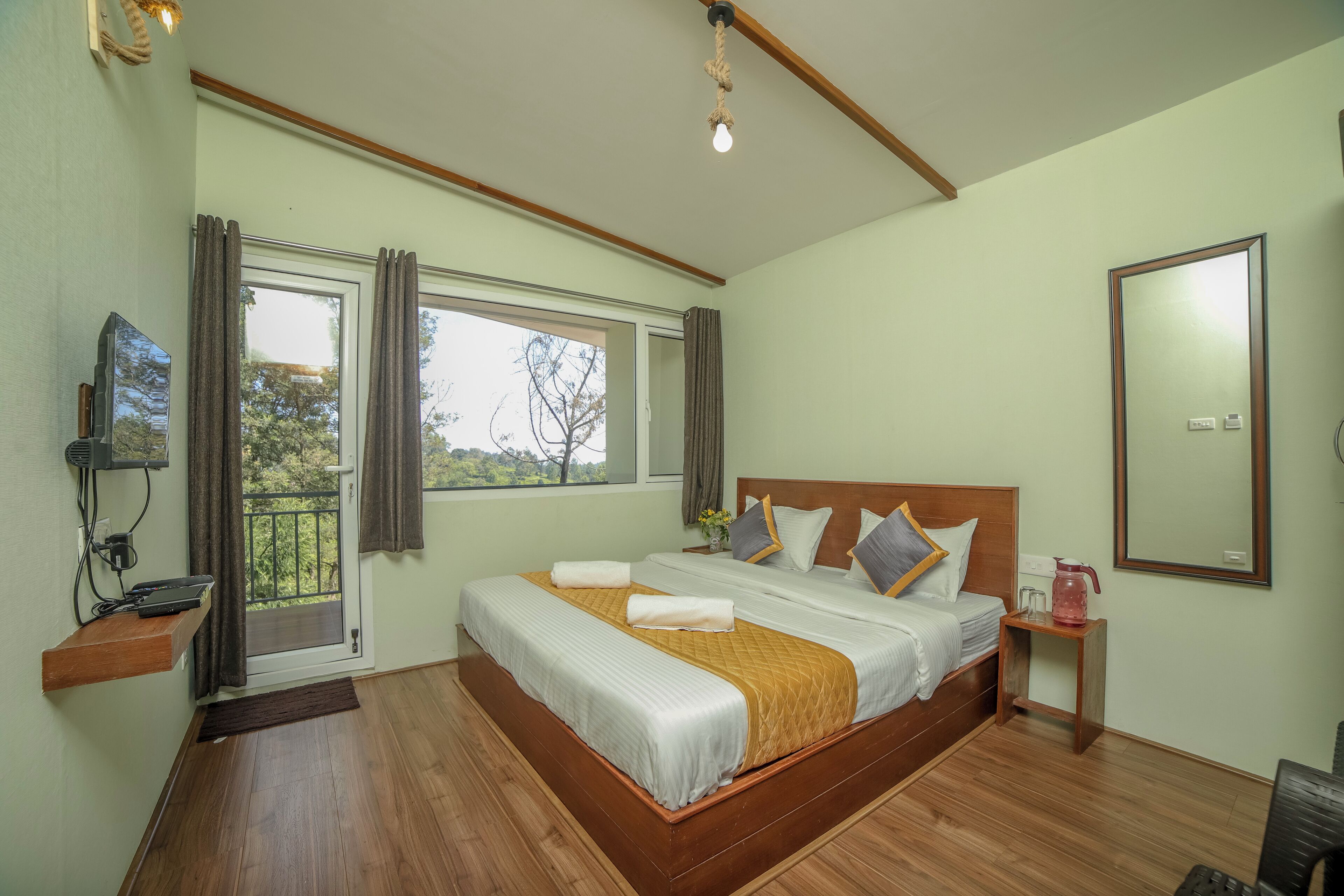Une chambre à coucher avec un lit en bois, une table de chevet avec une lampe, une fenêtre avec des rideaux et un téléviseur fixé au mur.