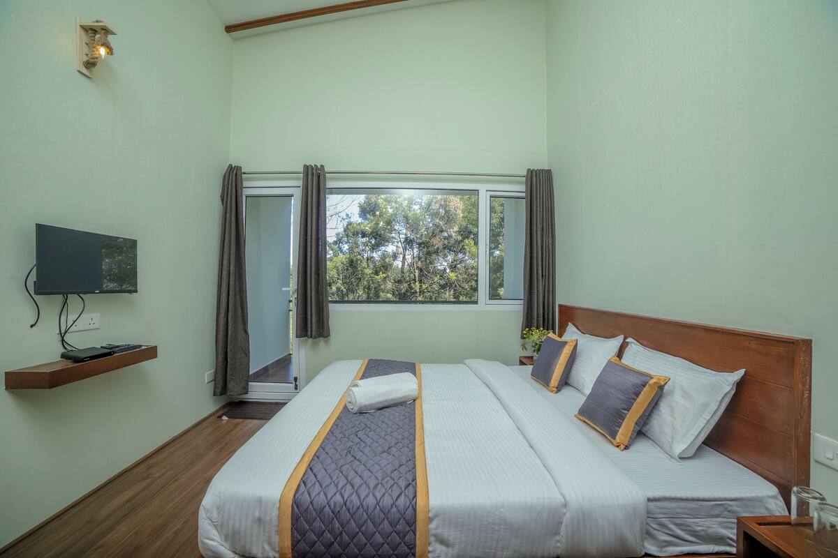 Une chambre bien rangée, avec un lit, un téléviseur posé sur une étagère et une fenêtre avec des rideaux.