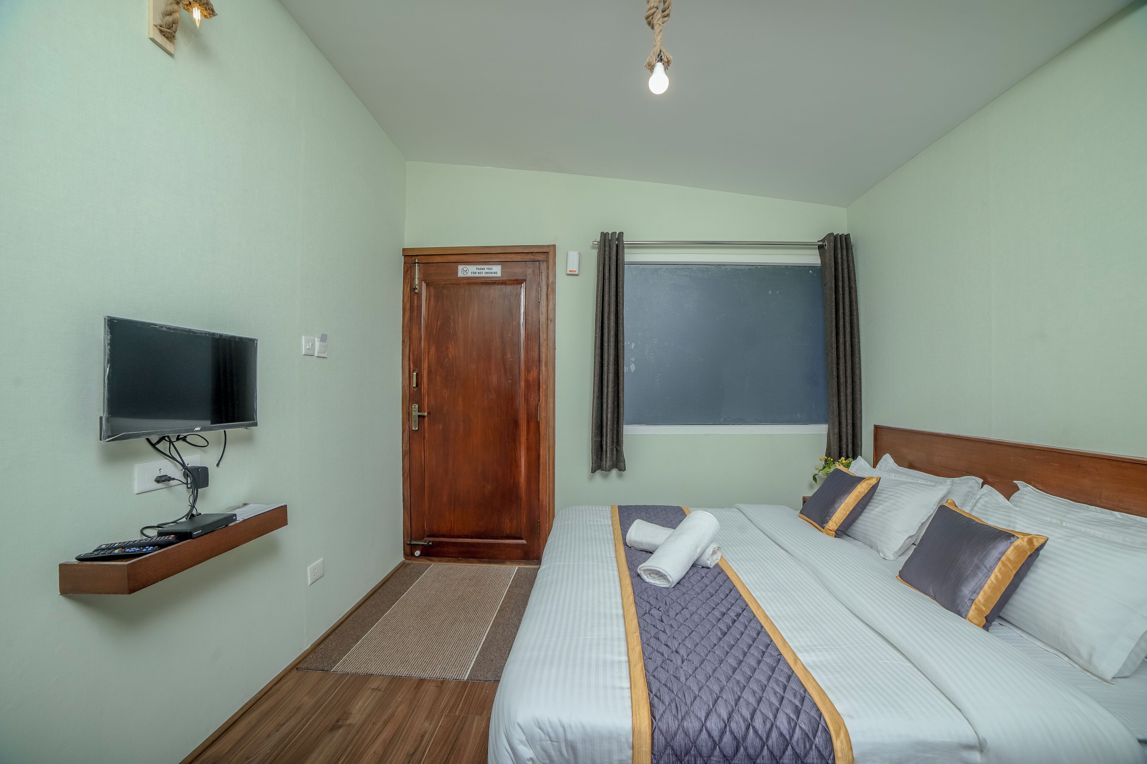 A hotel room with a bed, a television, a wooden door, and a window with curtains.