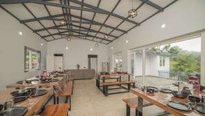 A spacious dining area with multiple tables and benches, a high ceiling with exposed beams, and large windows offering views of the outdoors. - Wattle Grove Resort (Kotagiri)