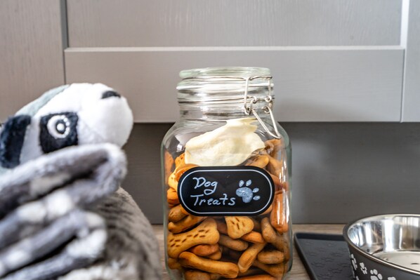 A glass jar labeled "Dog Treats" filled with various dog treats, placed on a kitchen counter next to a metal bowl. - The Ebor House - sleeps 7 guests in 3 bedrooms with hot tub (York)