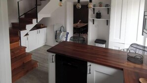 Une cuisine moderne avec un îlot central en bois, des armoires blanches et un lave-vaisselle noir. Un escalier en bois mène à un autre niveau.