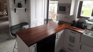 Une cuisine compacte avec des meubles blancs, un plan de travail en bois et un lave-vaisselle encastré. Des lampes suspendues et un four à micro-ondes sont fixés au-dessus du plan de travail.