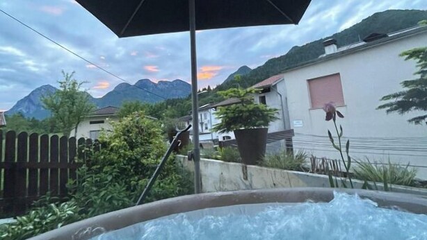 Un bain à remous avec vue sur les montagnes et une maison en arrière-plan.