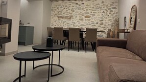 Ein gemütlicher Wohnbereich mit Steinwand, Holzboden und braunem Sofa, sowie ein Esstisch mit Stühlen.