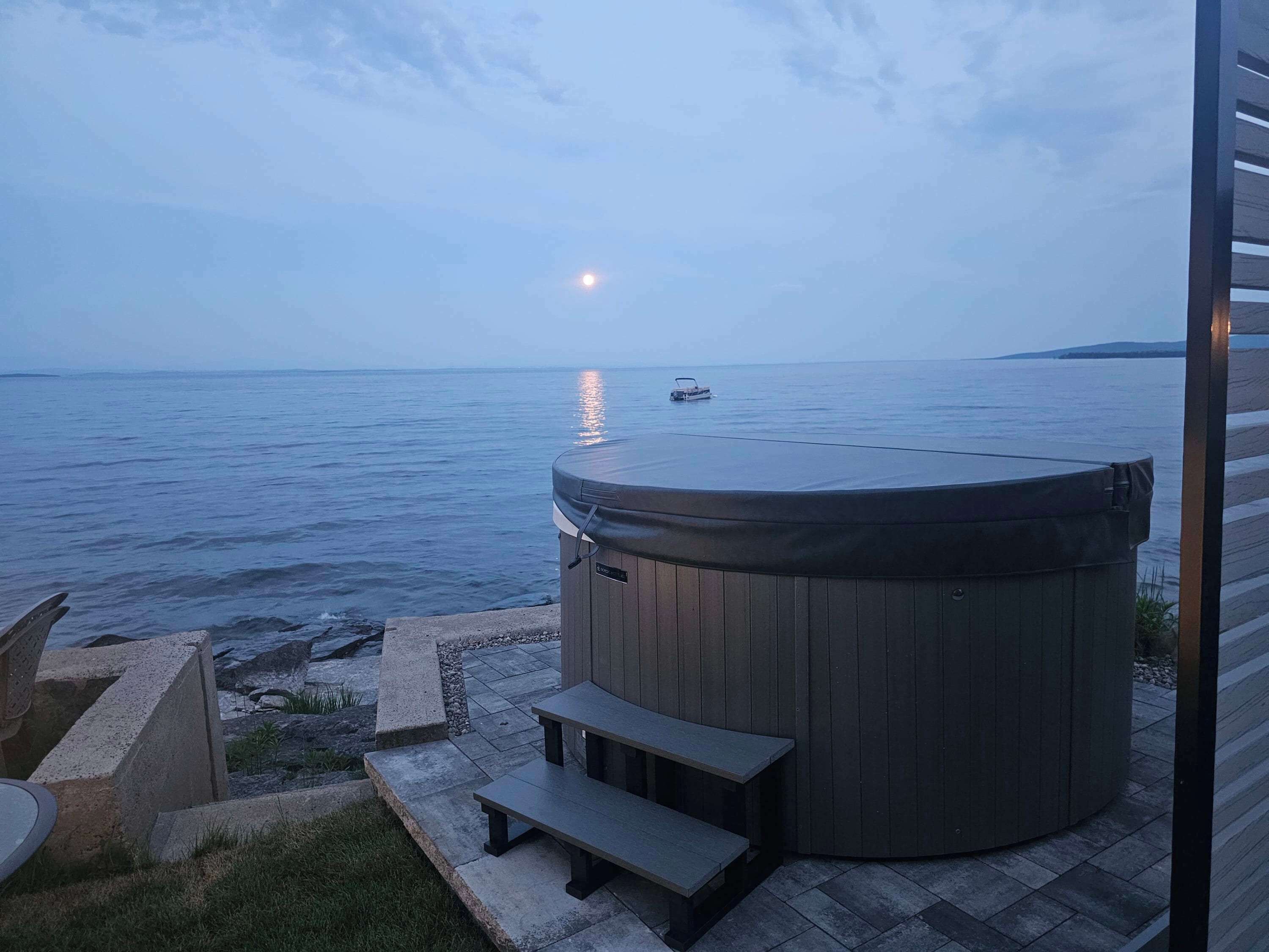 A hot tub on a patio with a view of the sea and a boat in the distance.