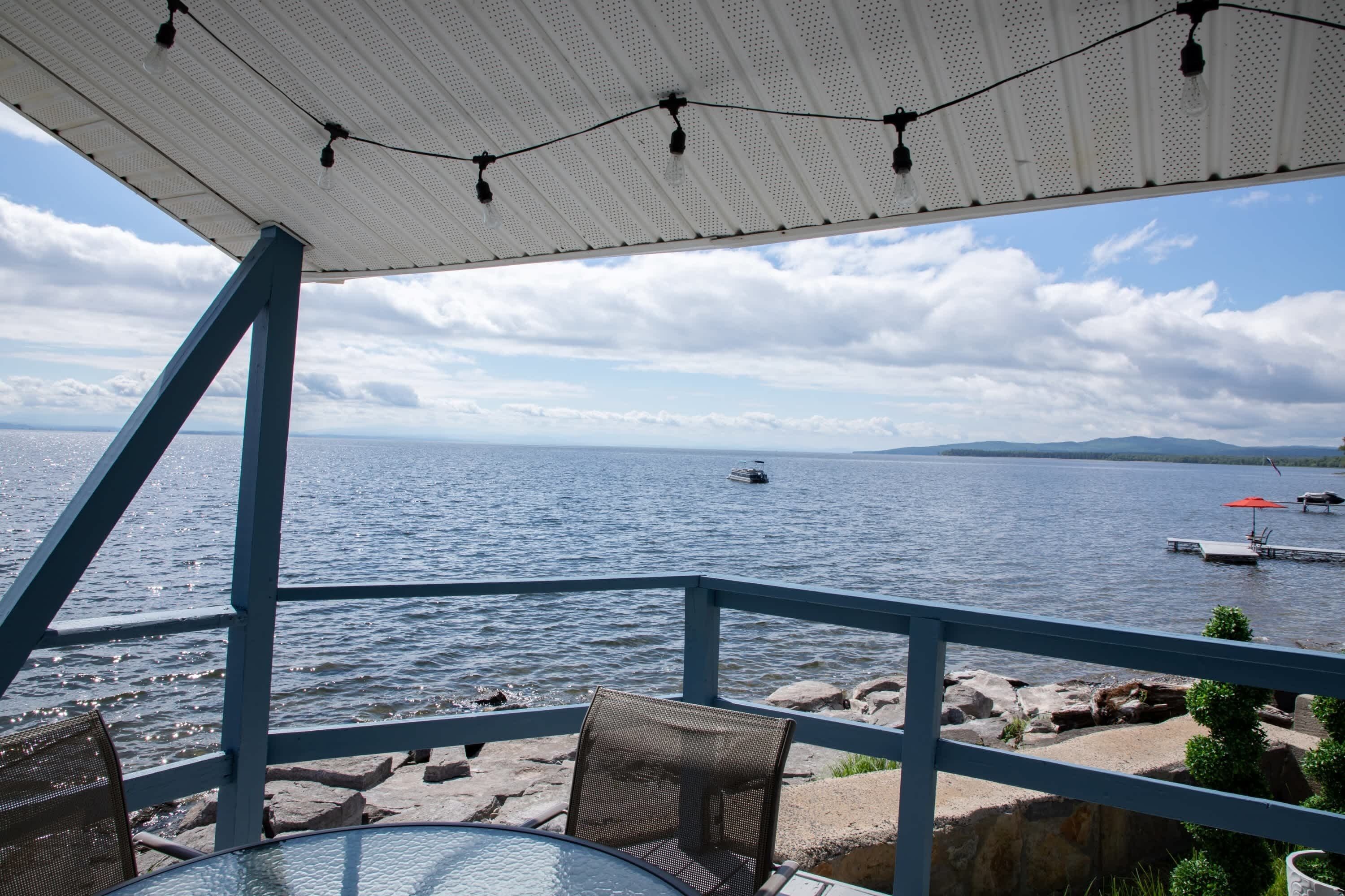 A table and chairs under a covered area with a view of a lake and distant mountains.