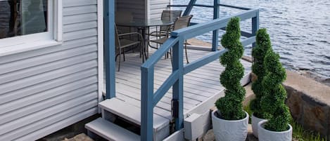 A house with a dock extending into a lake, a deck with chairs, and two potted trees.