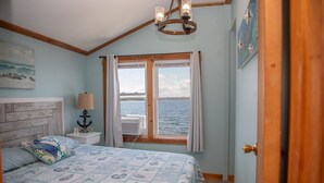 A bedroom with a bed, a nightstand, a lamp, a window with curtains, and a view of the sea. - ZaLo House Waterline cabin with Hot Tub Pets (Peru)