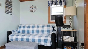 A room with a checkered sofa, a small ottoman, a wall clock, a lamp, and a shelf with items. - ZaLo House Waterline cabin with Hot Tub Pets (Peru)