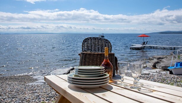 A wooden table with plates, glasses, and a bottle, set against a scenic lake view. - ZaLo House Waterline cabin with Hot Tub Pets (Peru)