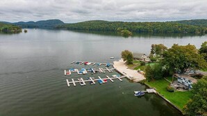 A lakeside view with a dock and boats, surrounded by hills and a house. - Remodeled, Family-Friendly Home in Private Community on Candlewood Lake (New Fairfield)